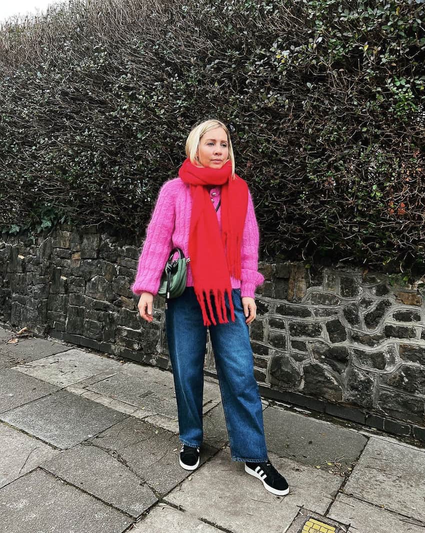 woman wearing a bright red scarf with a hot pink cardigan, blue jeans, and sneakers