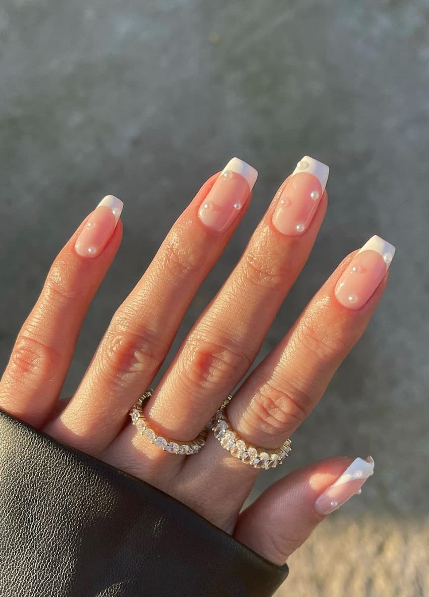 image of a hand with a classic pink and white manicure with white pearl jewel accents