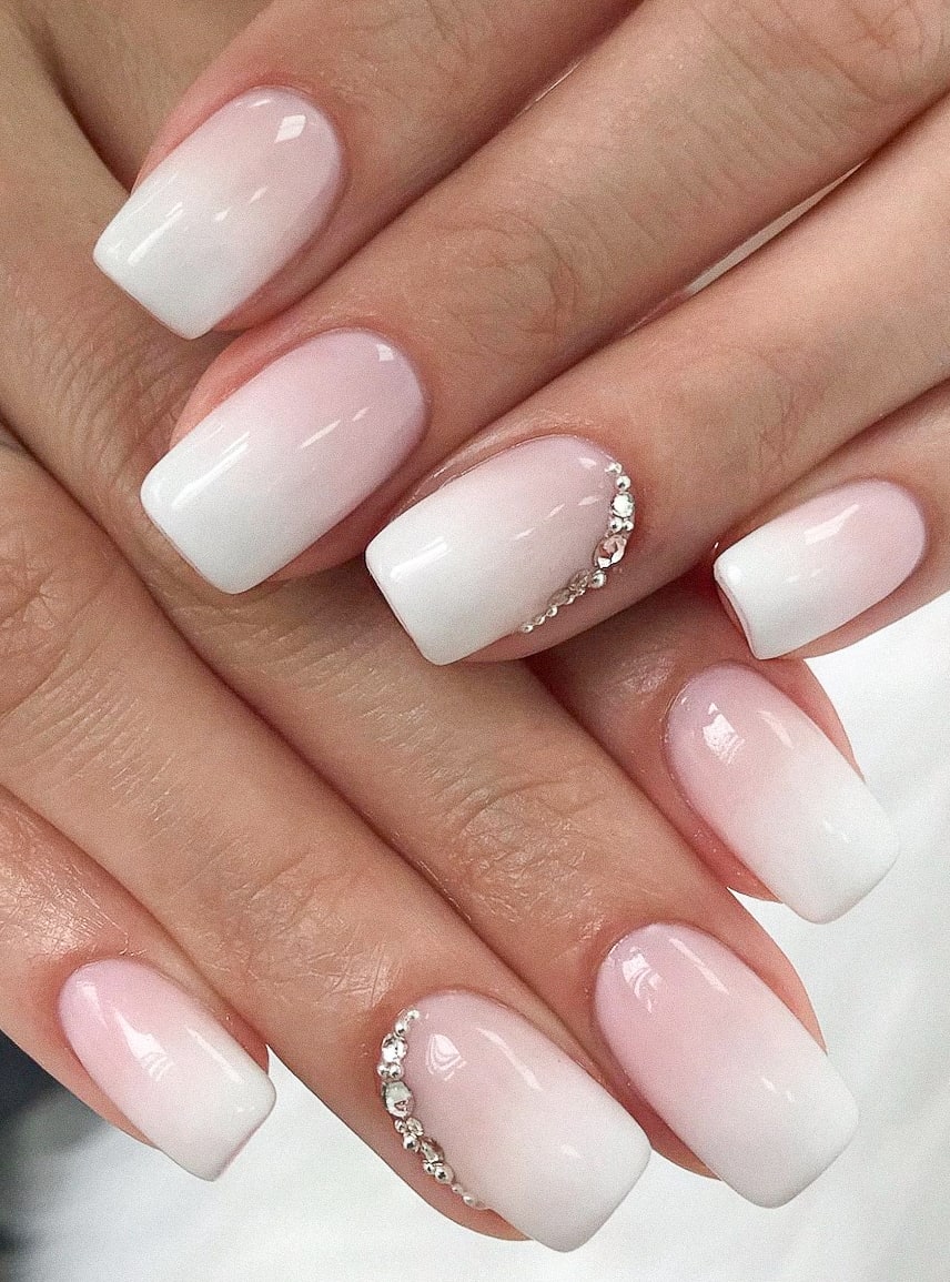 image of a pair of hands with classic pink and white ombre nails with jewels at the cuticle