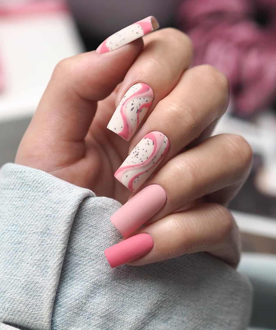 image of a hand with matte pink and white nails with wave and speckled designs
