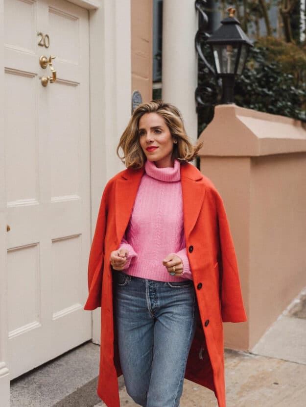 woman wearing a red wool coat over a bright pink sweater with jeans