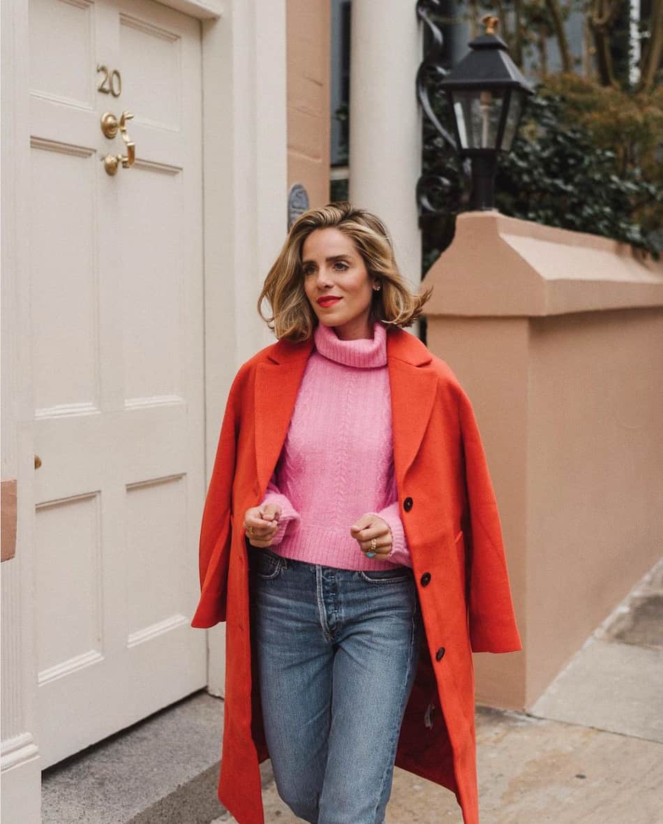 woman wearing a red wool coat over a bright pink sweater with jeans