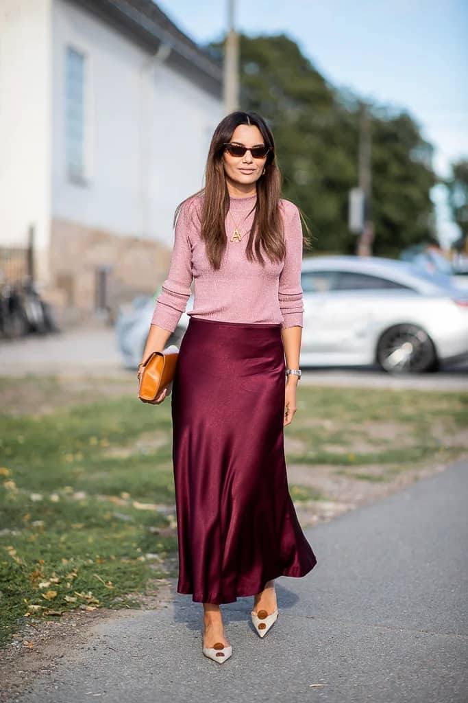 woman wearing a light pink sweater with a red burgundy silk midi skirt