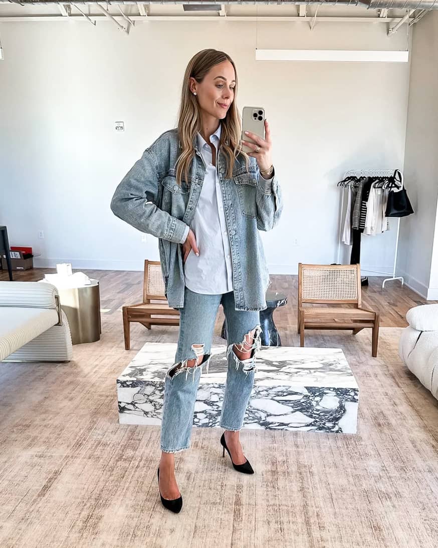 Woman wearing a denim shacket with a white button up, distressed jeans and black heels.