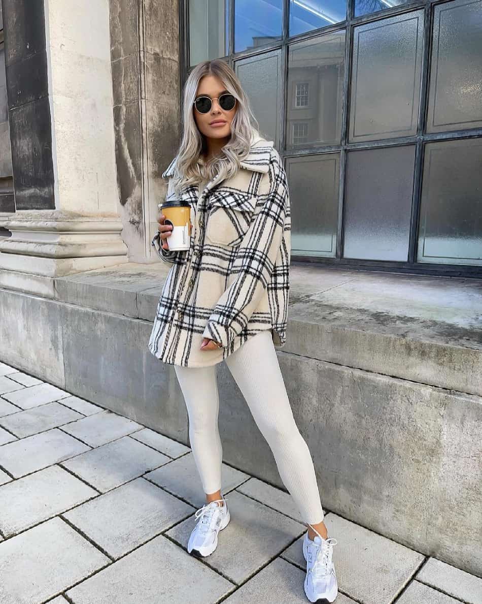 Woman wearing an oversized plaid shacket with white leggings and sneakers.