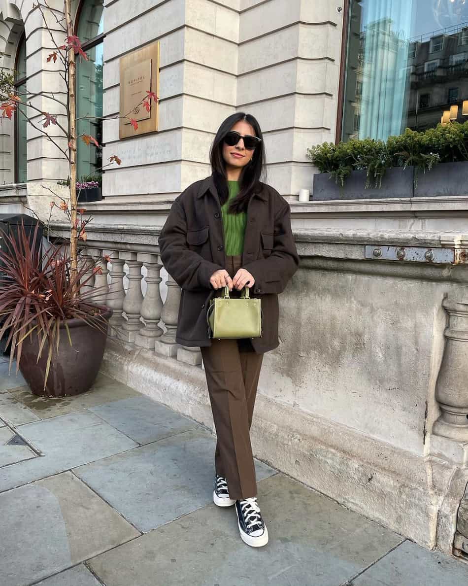 Woman wearing an oversized shacket with a green sweater, brown trousers and sneakers.