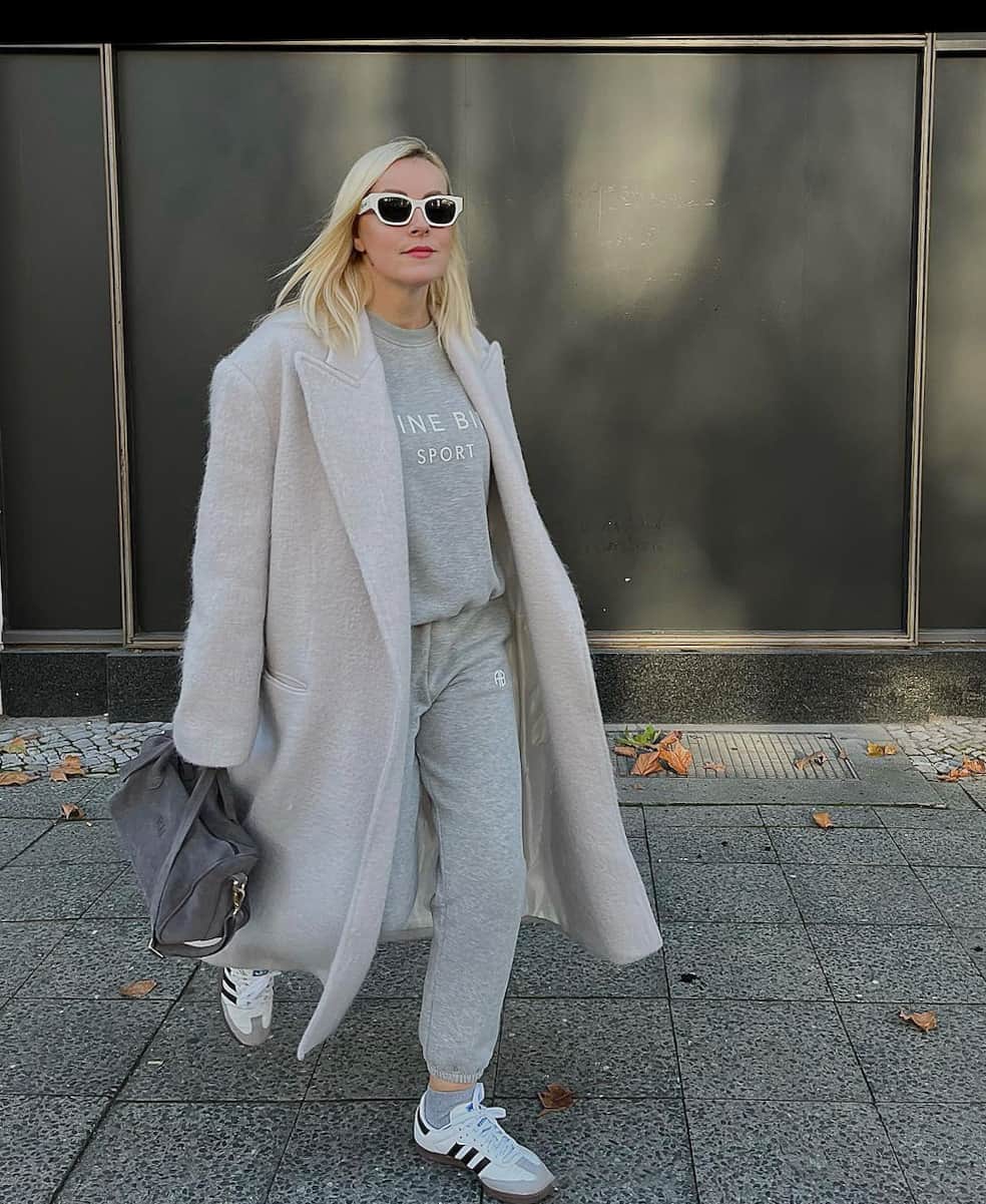woman wearing a matching grey sweatshirt and sweatpants with a long ivory wool coat over, and white sneakers 