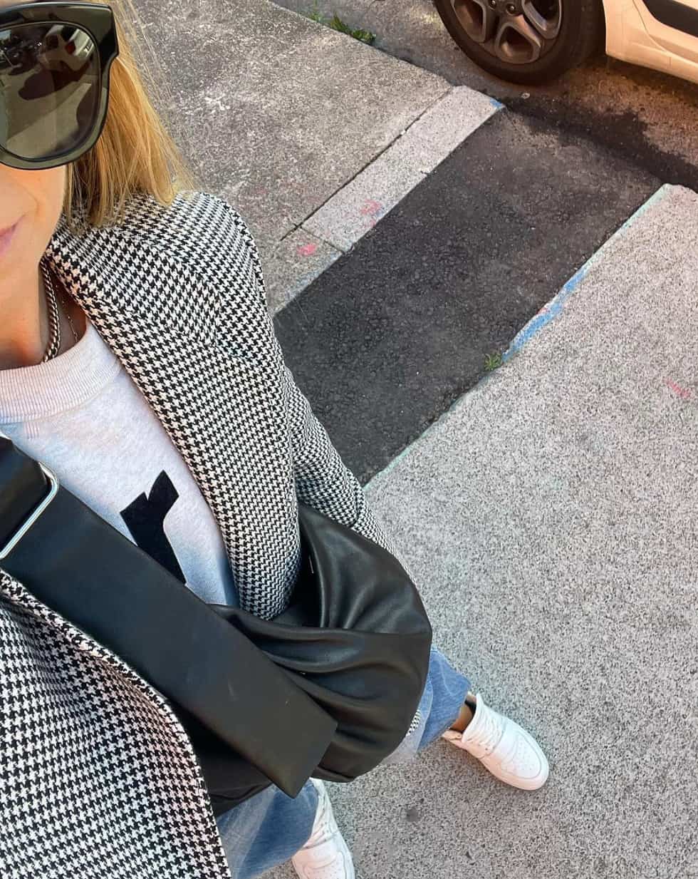 overhead selfie of a woman in a houndstooth blazer over a grey sweatshirt, jeans, and sneakers