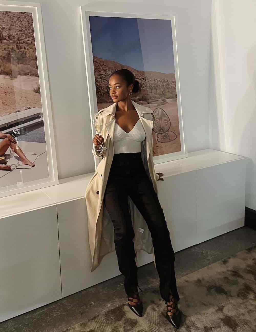 Black woman wearing a long tan trench coat over a white top and black pants with heels