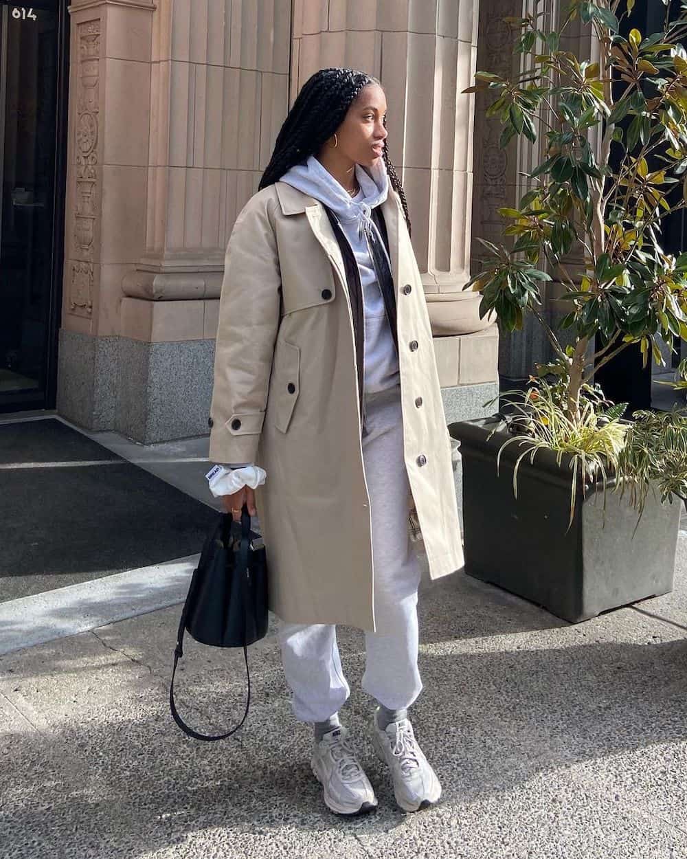Black woman wearing a light tan trench coat over a grey sweatsuit with sneakers