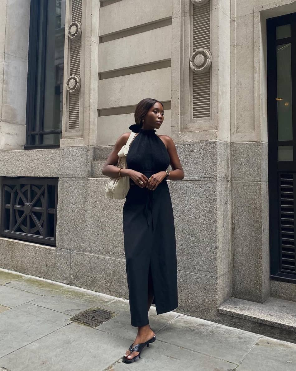 chic black woman wearing a sleeveless black blouse with a long black skirt and pointed heeled mules