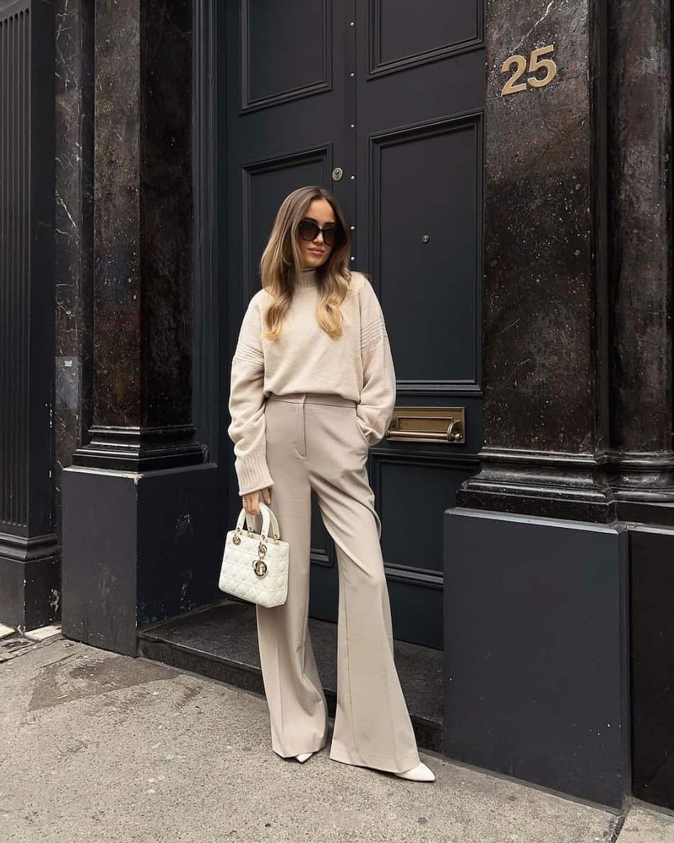 woman wearing a beige knit sweater with wide leg beige trousers and white heels