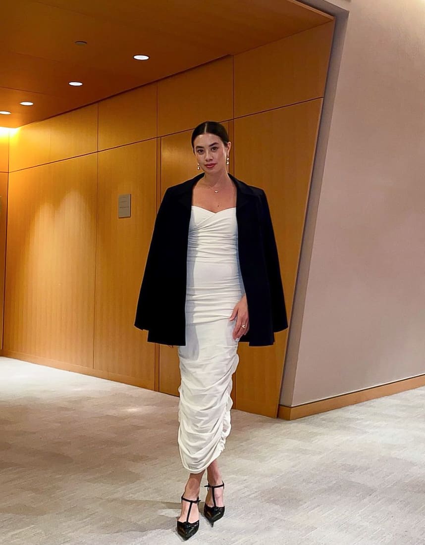 woman at the ballet wearing a black blazer over a long white ruched dress and black heels