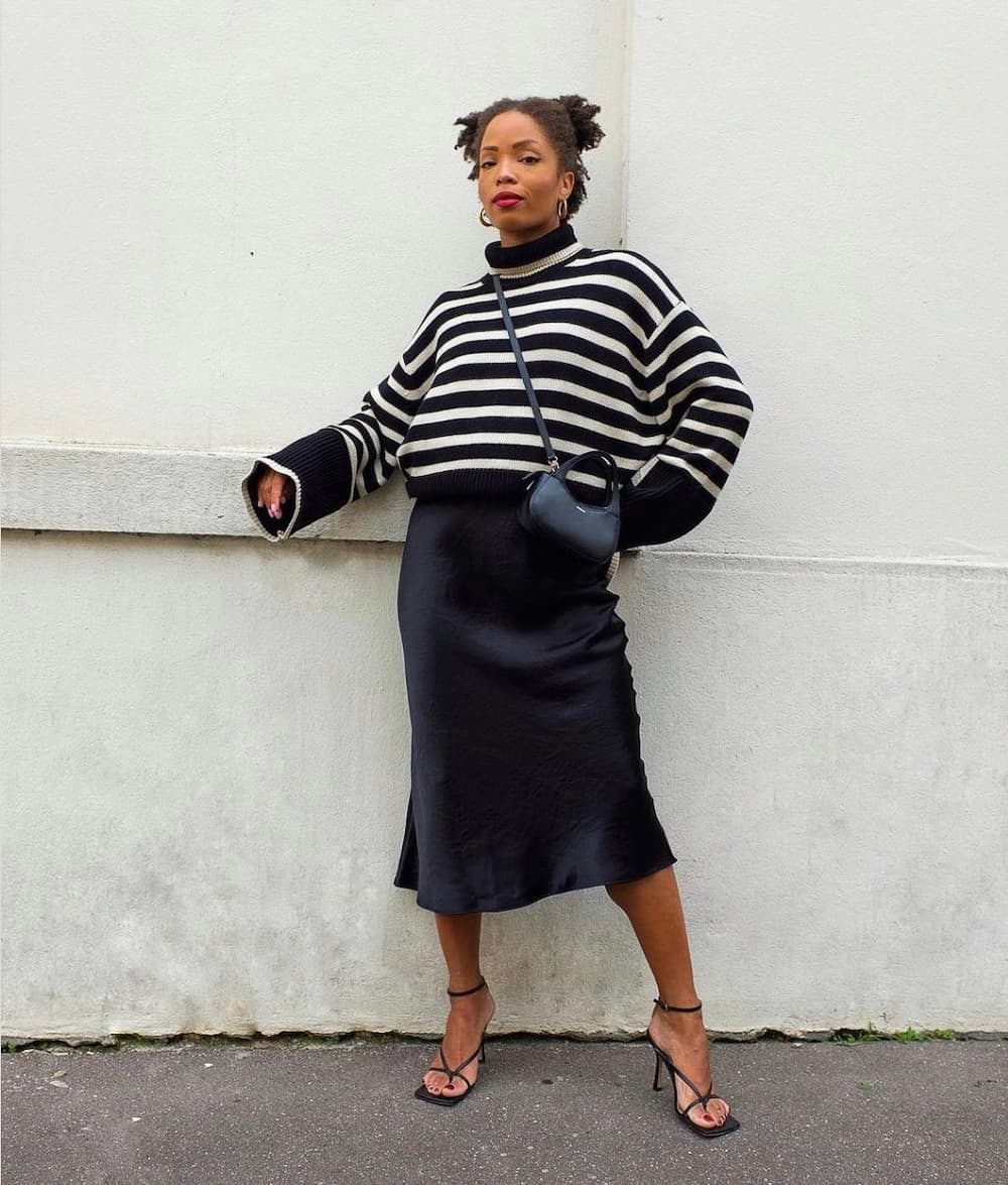black woman wearing an oversized striped knit sweater with a black midi slip skirt and dainty black heeled sandals