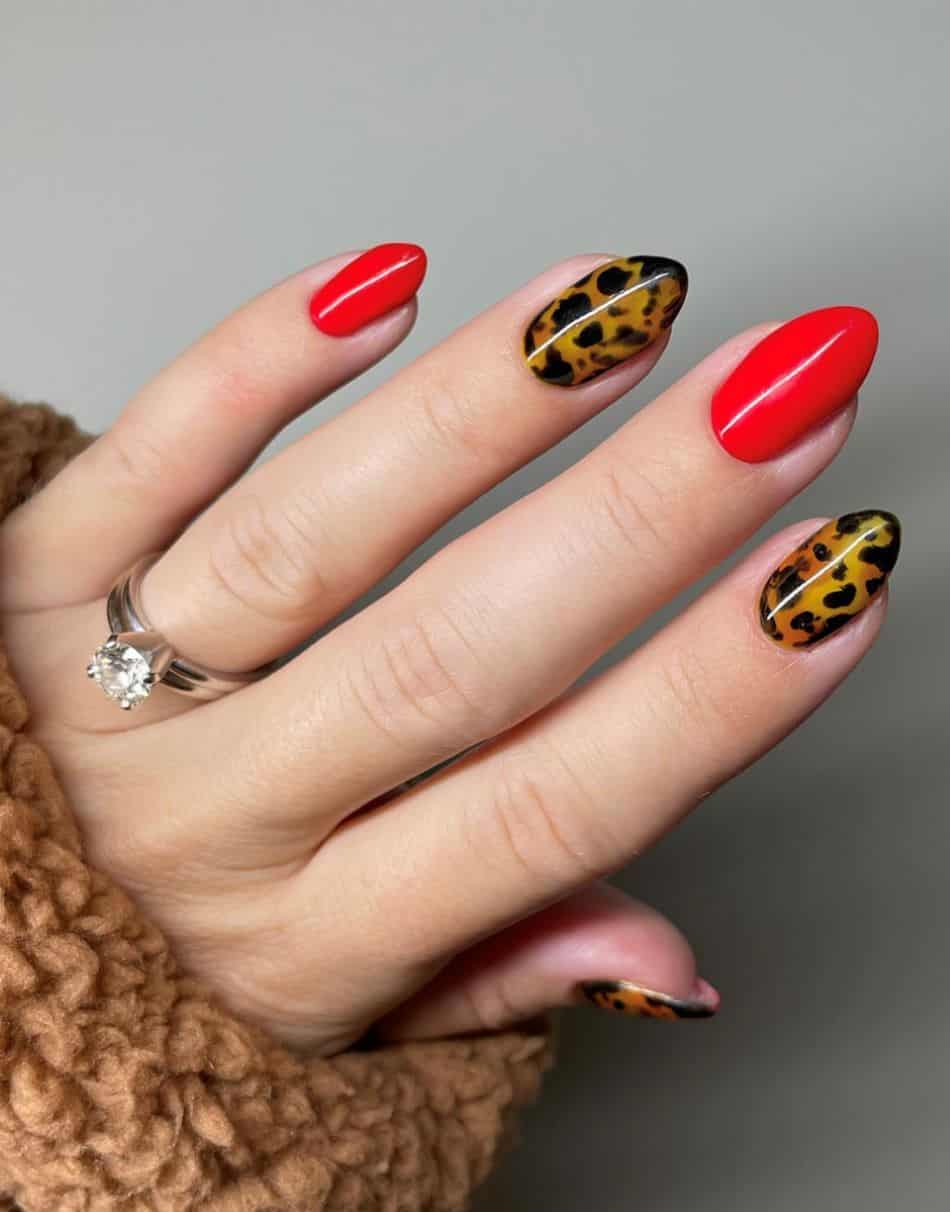 An image of a hand with 90s nail designs using bright red nail polish and tortoise shell print nails