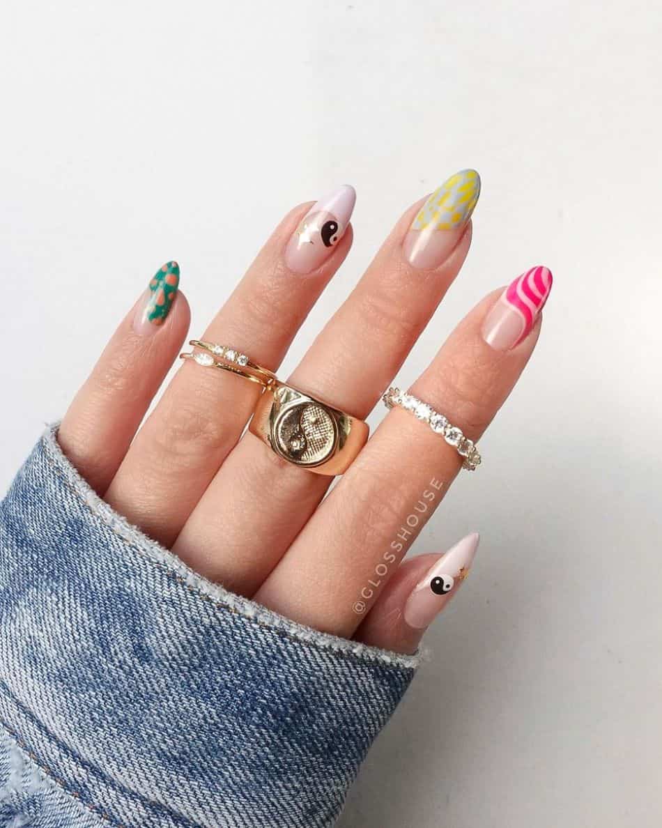 An image of a hand with 90s nail designs like waves, polka dots, and yin and yang stickers