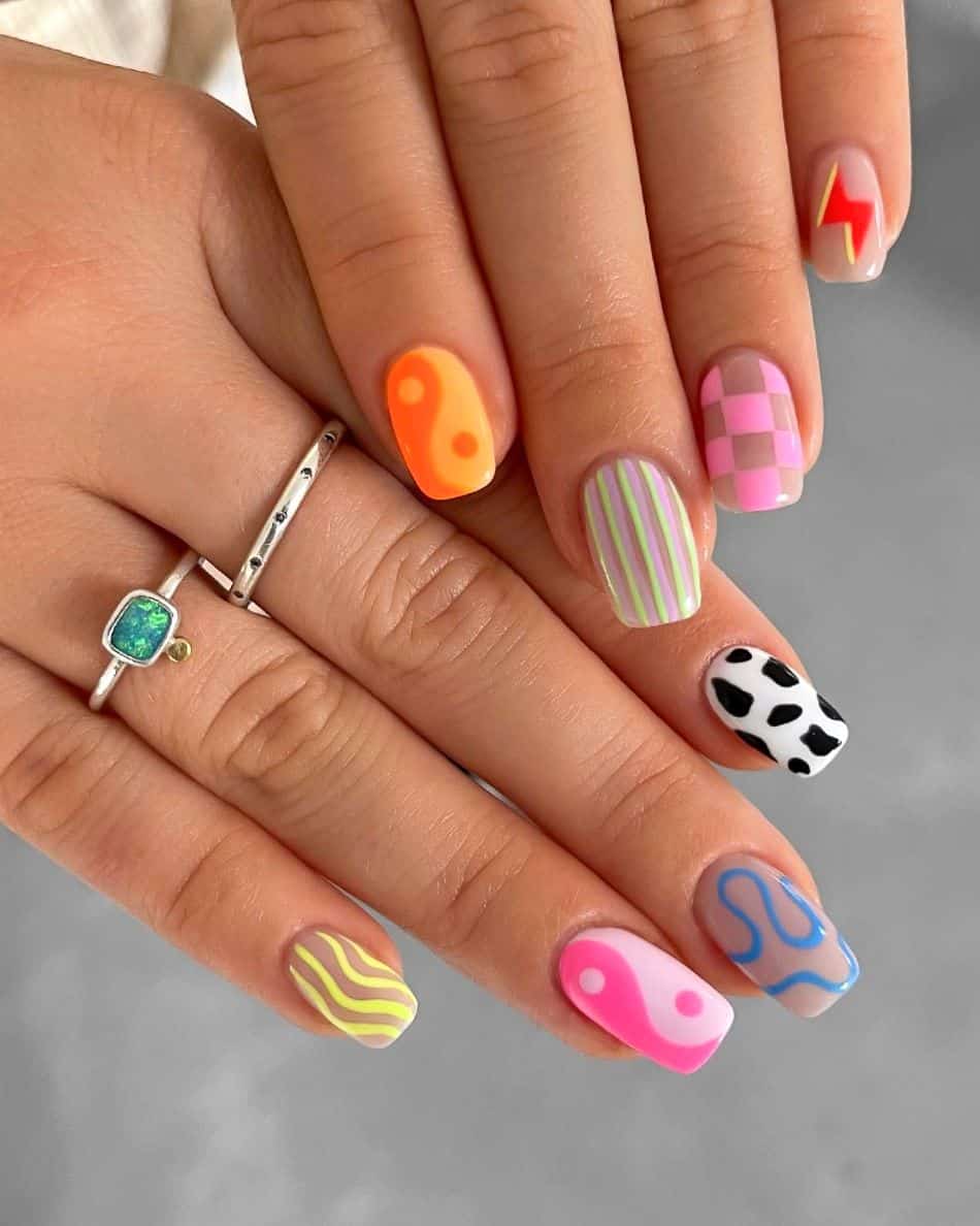 An image of a hand with 90s nail designs such as checkerboard, yin and yang symbols, lightning bolts, and cow print