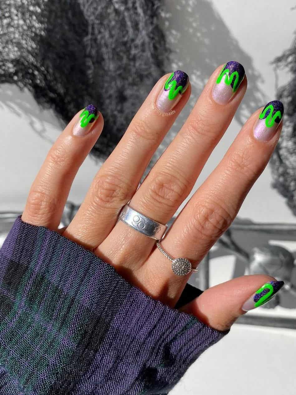 An image of a hand with goosebumps inspired nails featuring purple glitter nail tips and wavy green lines 