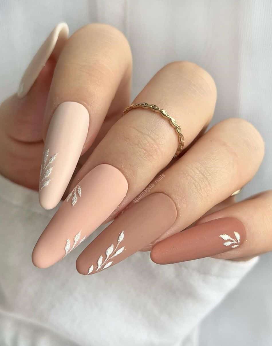 an image of a hand with gradient nails featuring beige and brown tones with sparkly white leaf art