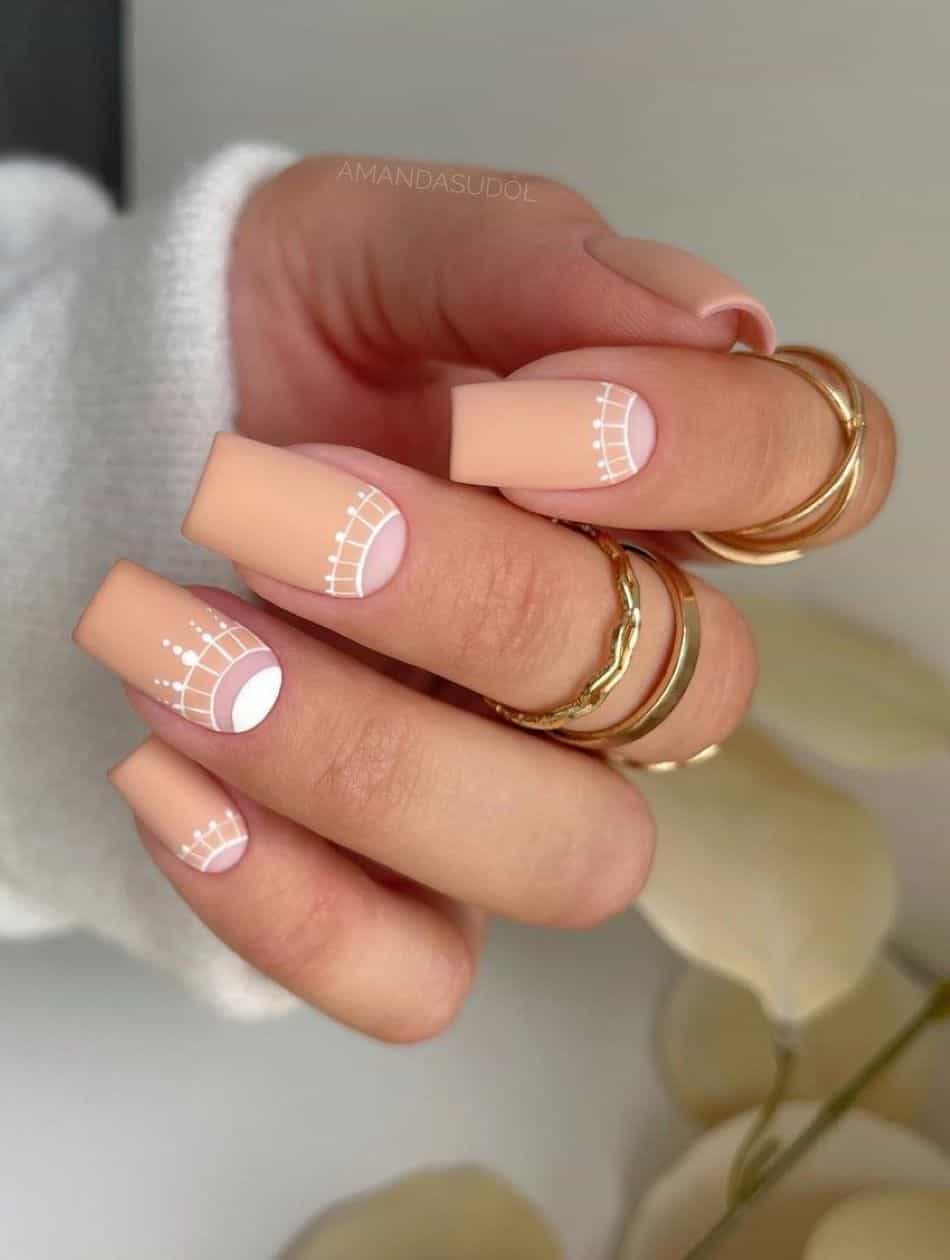 an image of a hand with matte beige nails, nude half-moons, and white accents