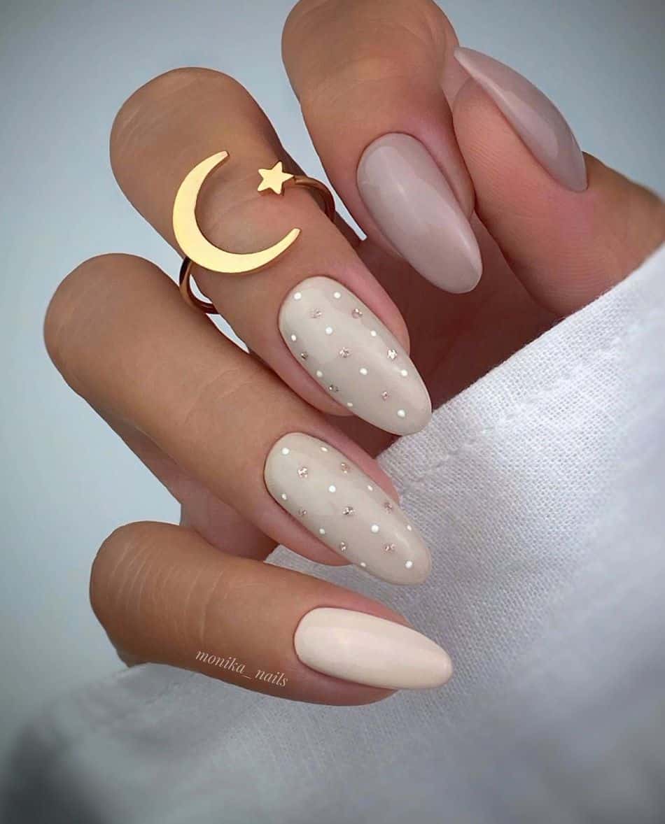 an image of a hand with different shades of beige and accent nails featuring white and silver polka dots