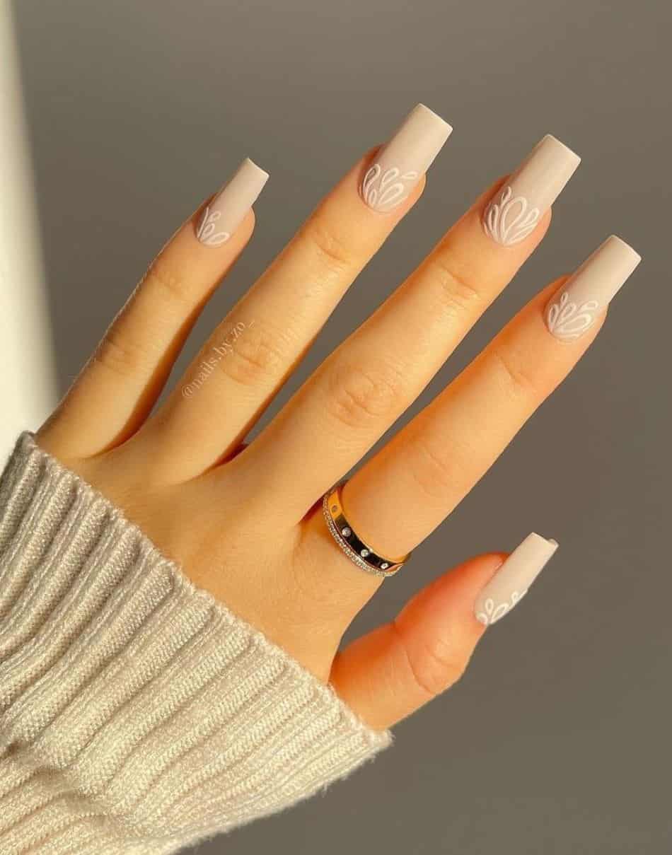 an image of a hand with square beige nails and white nail art