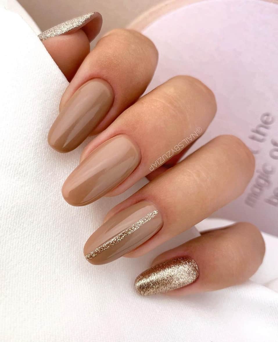 an image of a hand with beige nails and gold glitter accents