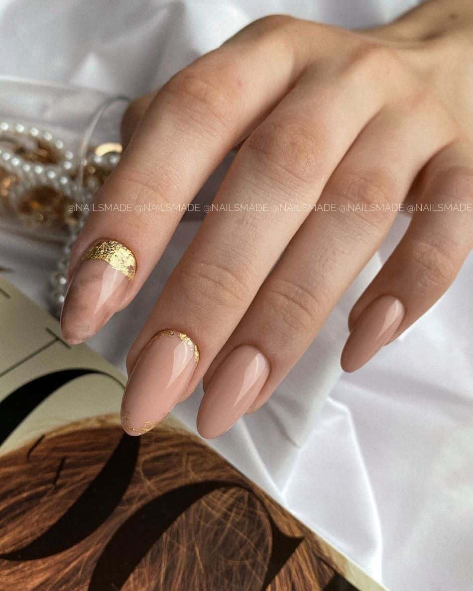 an image of a hand with beige nails with a marbled beige accent nail and gold leaf details