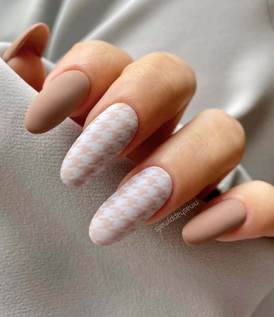 an image of a hand with solid beige nails and white and beige houndstooth print nails