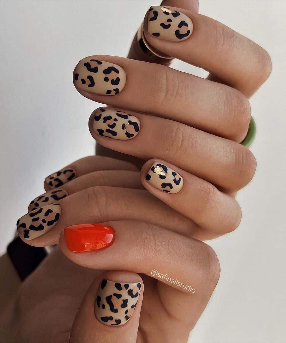 an image of a hand with short beige cheetah print nails and a red accent nail