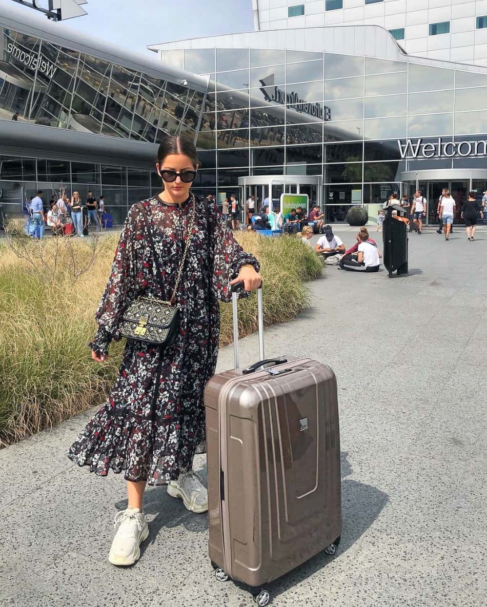 A woman at the airport with a flowing black floral maxi dress and chunky white sneakers