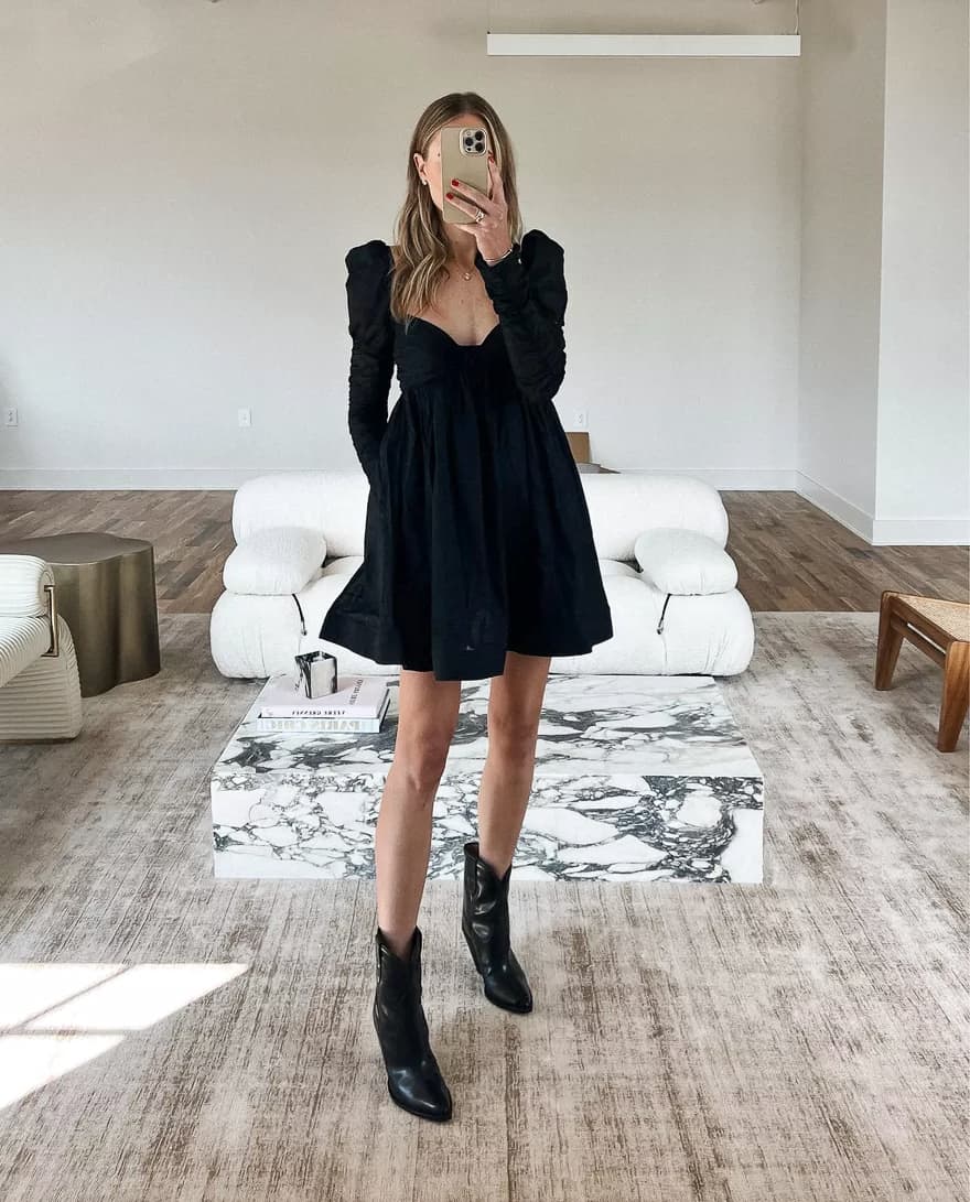 An image of a woman with a black baby doll style dress with long puffed sleeves and black ankle cowboy boots
