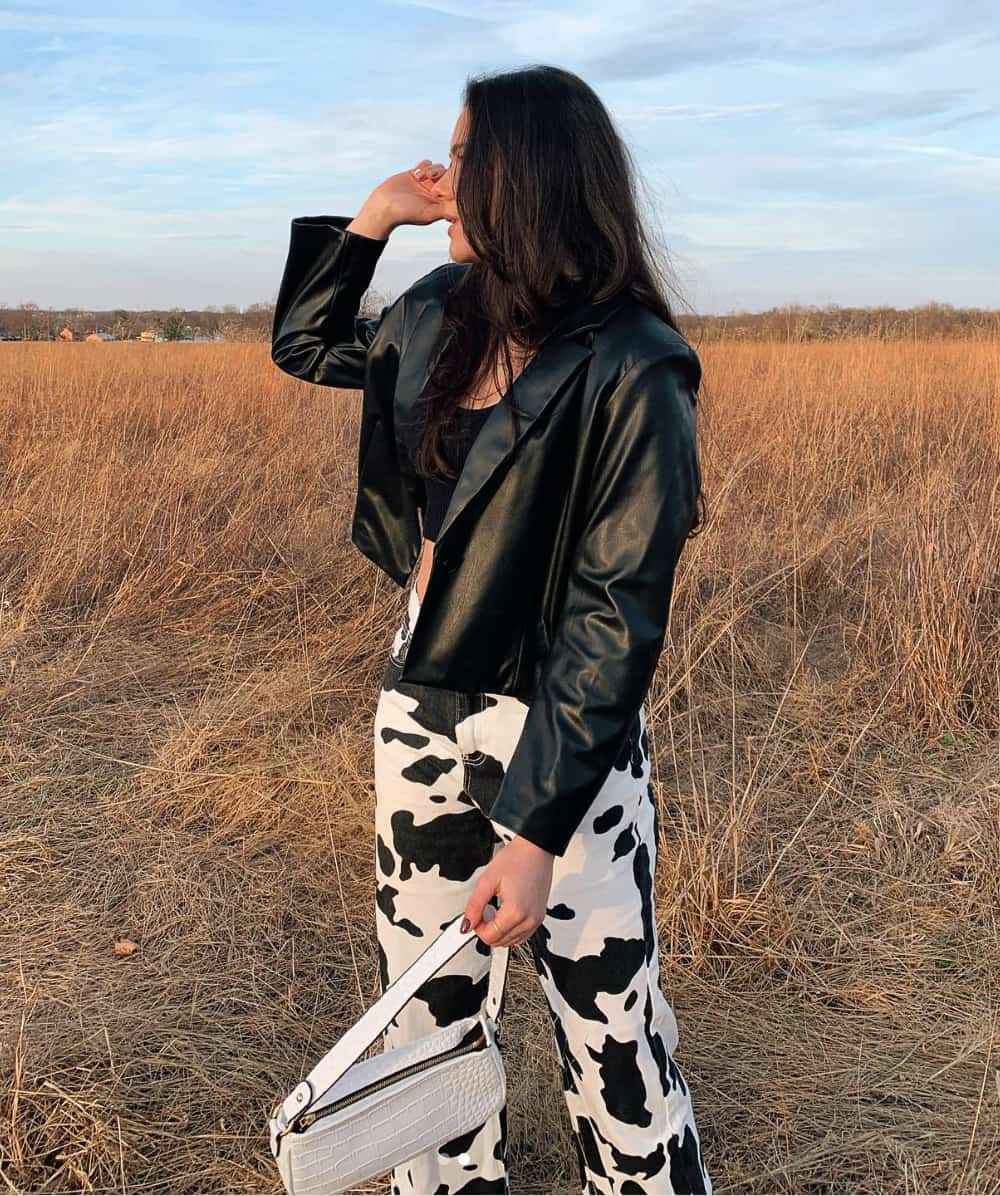 An image of a woman with cow print jeans, a cropped black tank, and a leather jacket