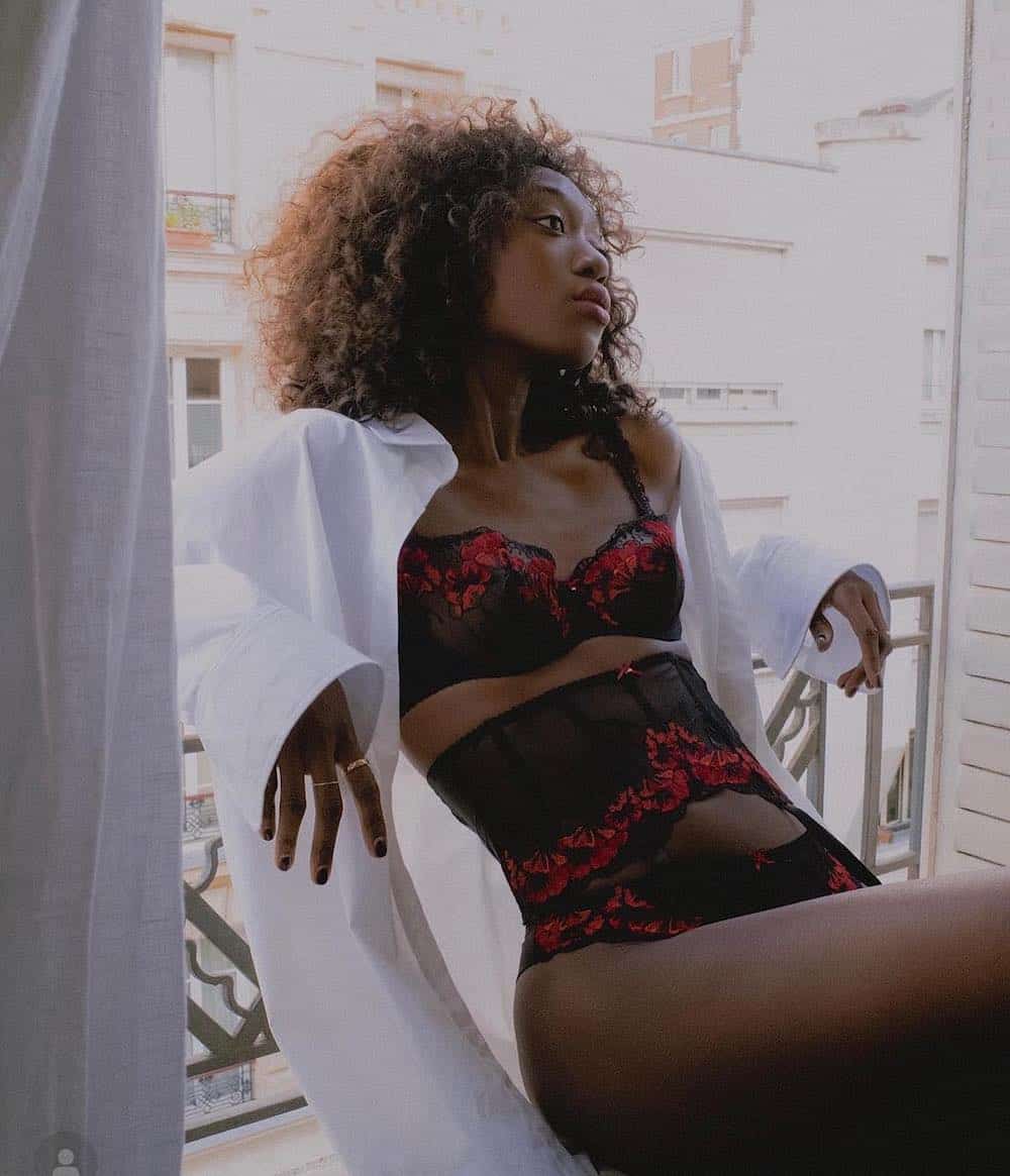 image of a Black woman wearing an oversized white cotton button up shirt over a red and black lingerie set