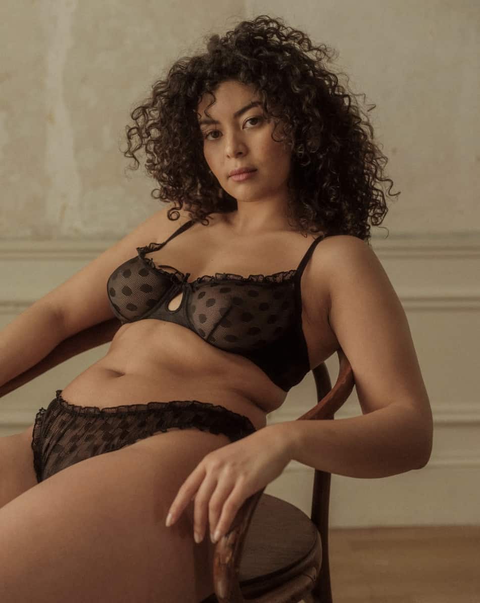 a mid-size Black woman wearing a sheer black bra and panties lingerie set