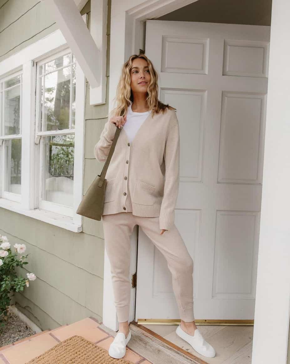 A woman wearing beige joggers, a white tee, and a beige cardigan with white slip-on sneakers