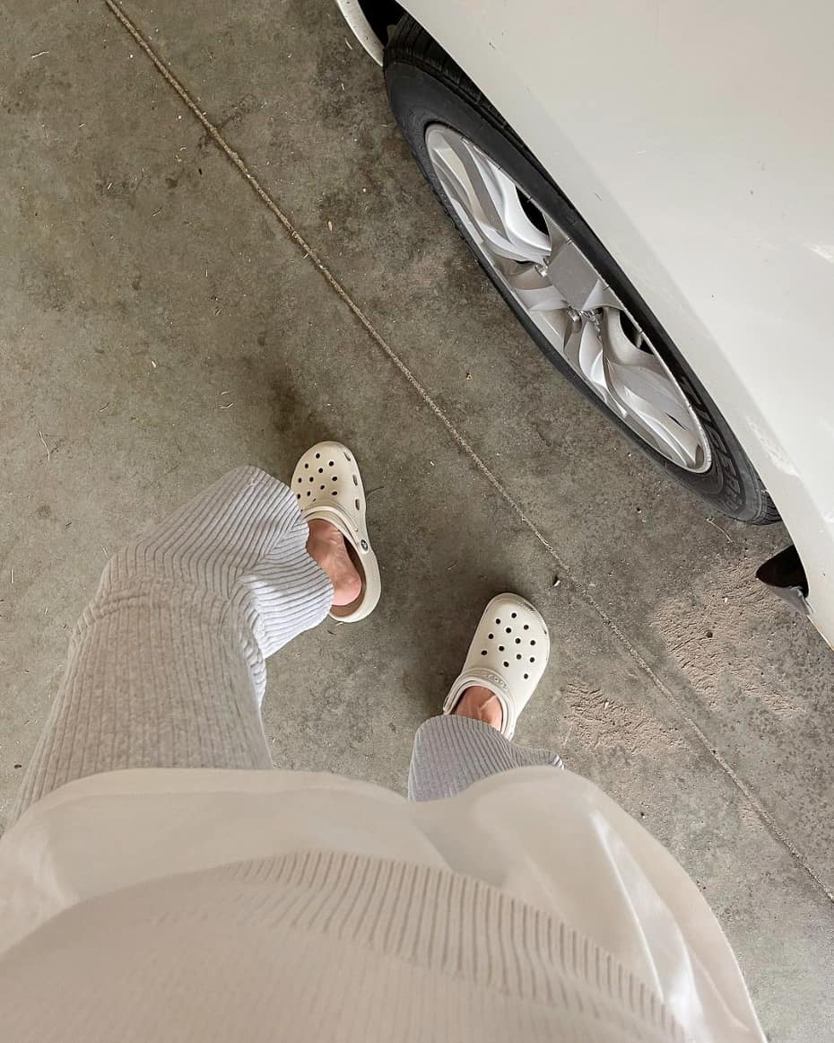 An overhead view of a woman wearing a sweater with light grey sweatpants and white clogs