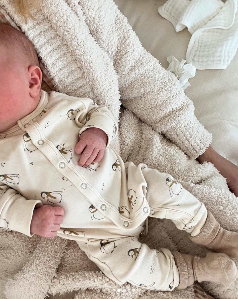 An overhead view of a woman wearing a beige terry set with her newborn baby resting on her