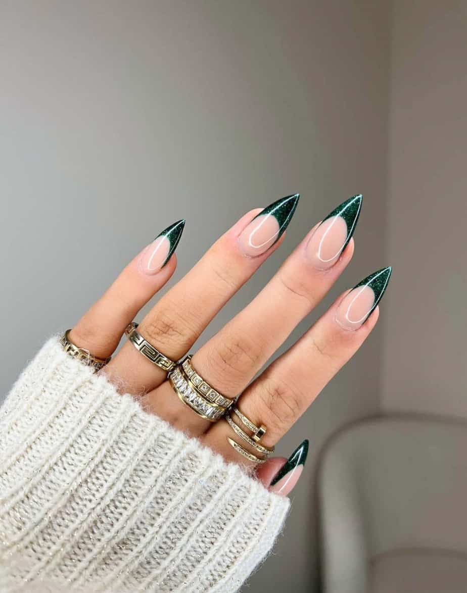 A hand with dark green glittery French tips on stiletto nails
