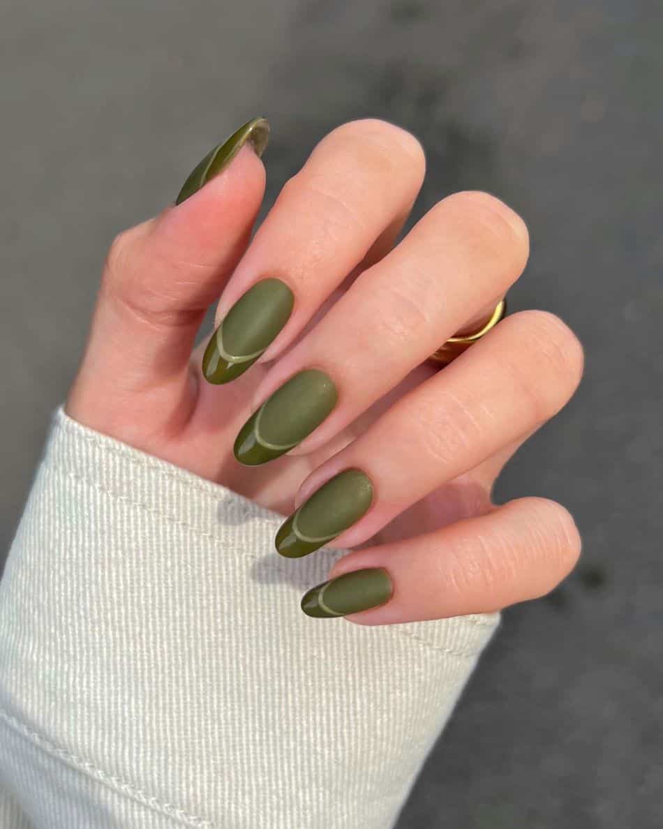 A hand with matte dark green nails and glossy green French tips