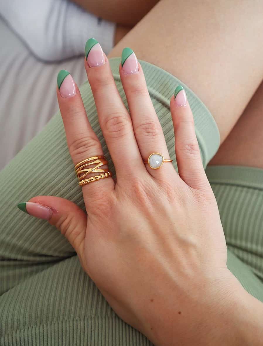 A hand with asymmetrical green French tips on long almond nails