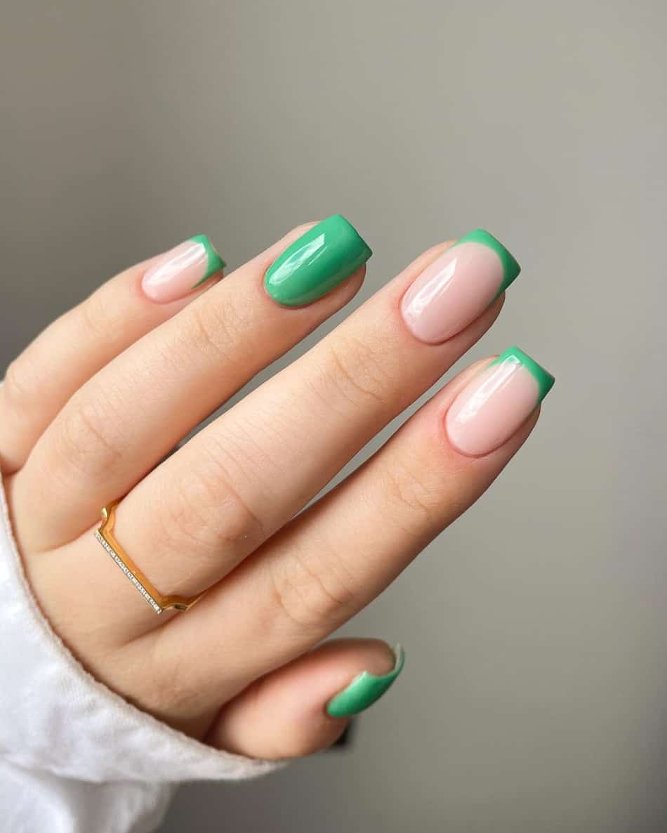 A hand with seafoam green French tips and solid-colored accent nails