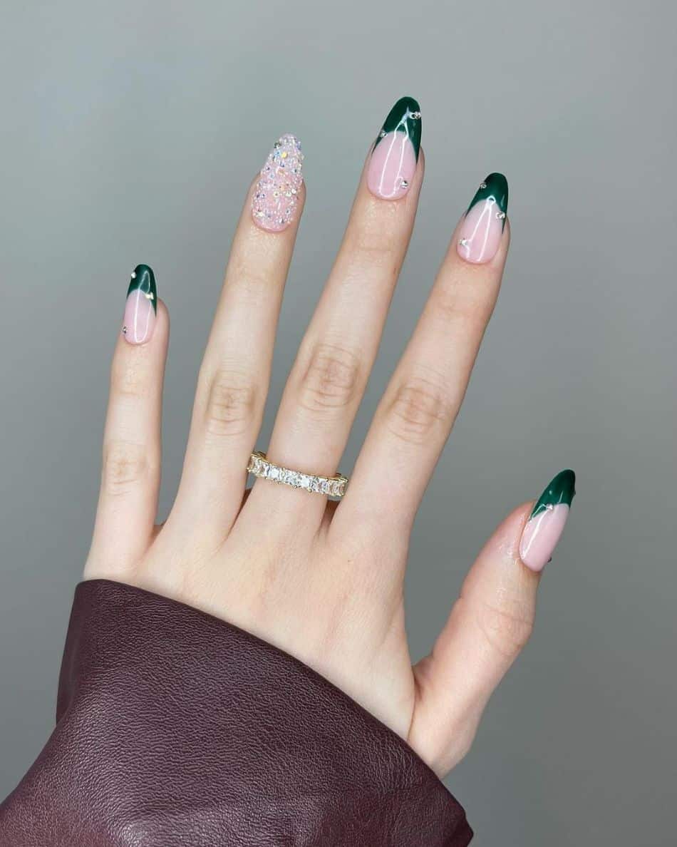 A hand with dark green French tips with gem accents and a gem covered accent nail