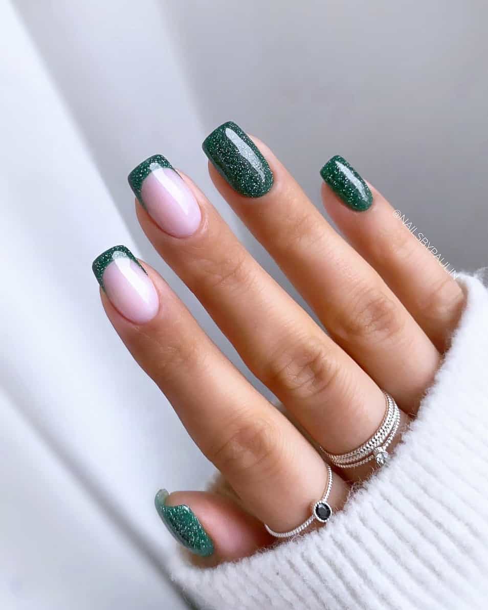 A hand with square nails featuring dark green glitter polish and green French tip nails