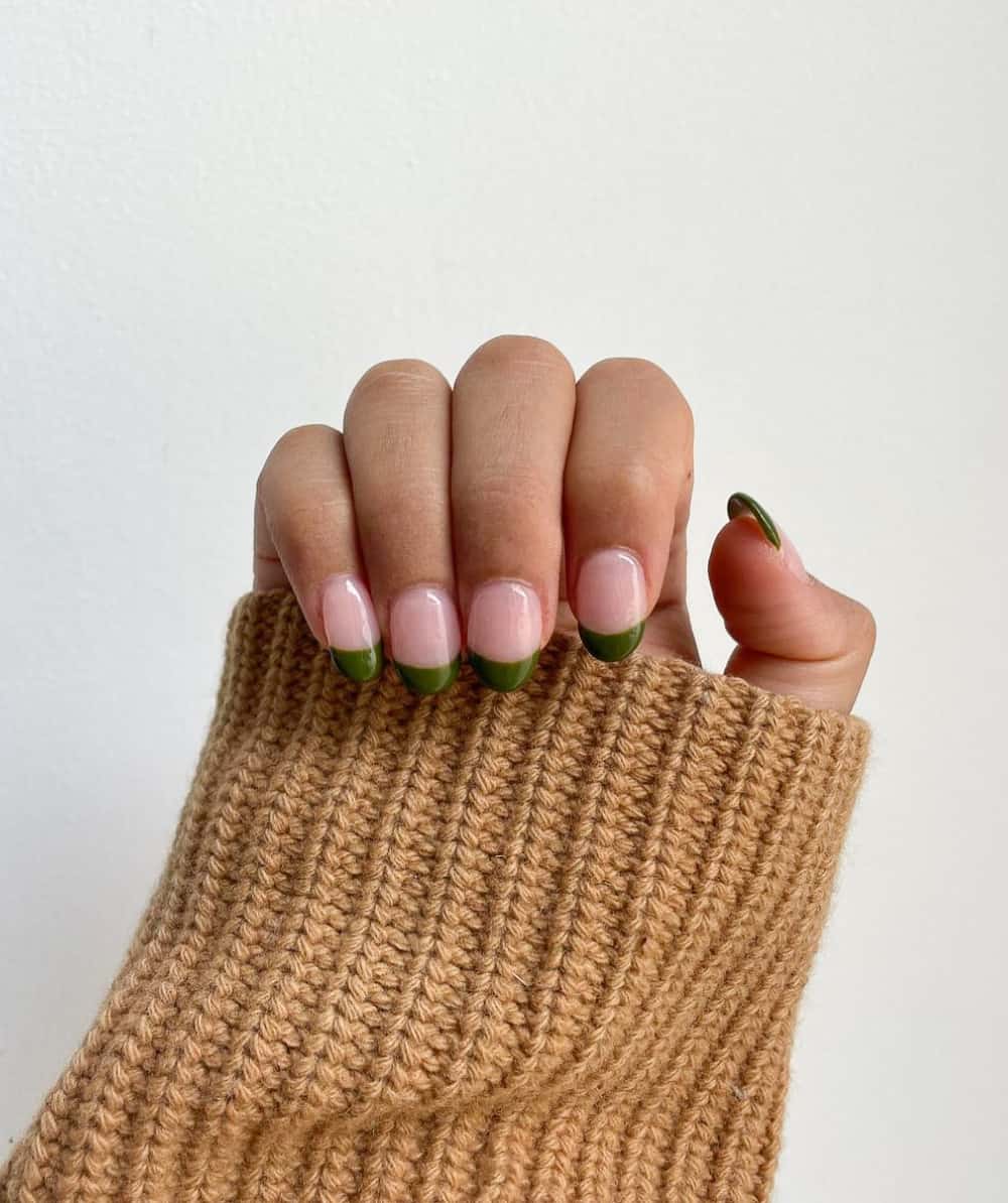 A hand with round nails featuring dark green French tips