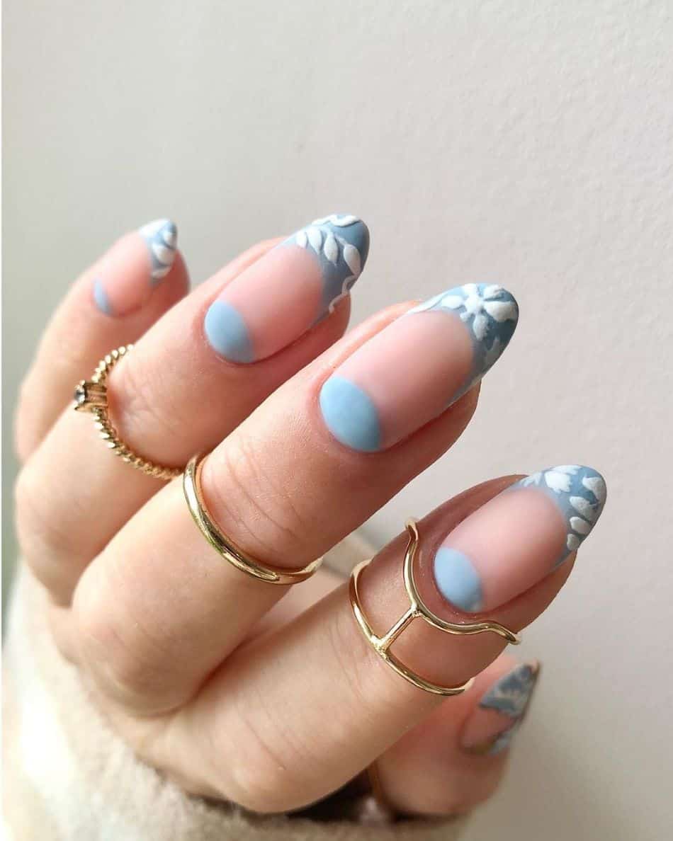 Matte almond nails with half-moons and light blue French tips with white flowers. 