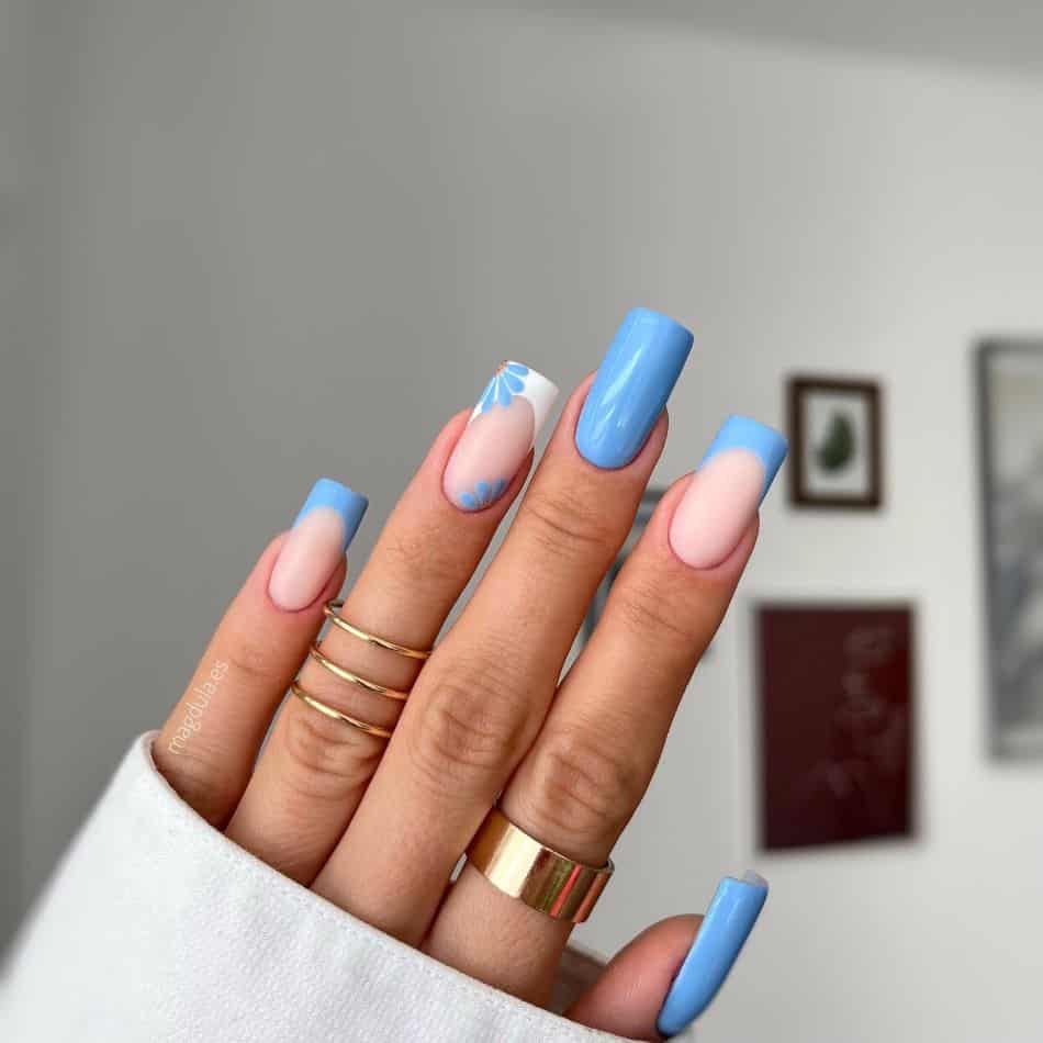 Square blue nails with French tip accents and floral details. 