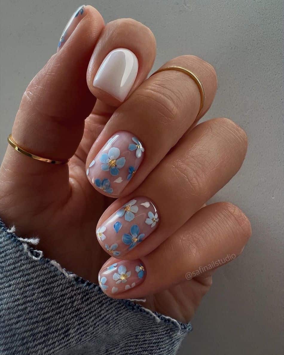 Short manicure featuring baby blue floral nail art with gold centers and white accent nail. 