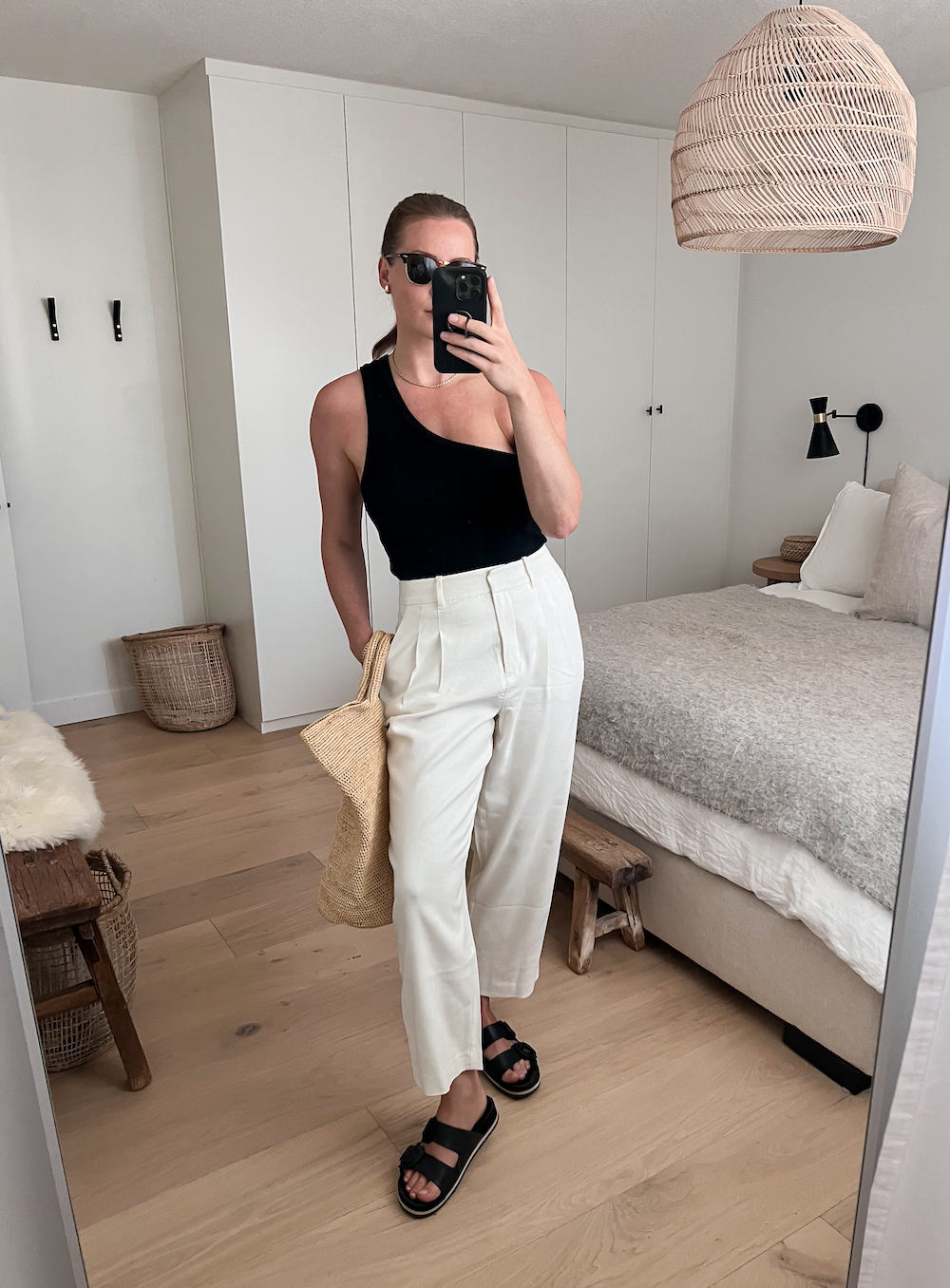 woman wearing a black asymmetrical tank top with white linen pants and black sandals