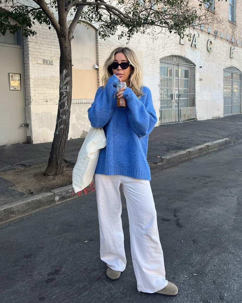 An image of a woman with white linen pants, a blue sweater, and a white tote bag